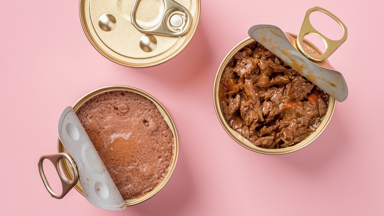 Wet cat food in cans on pink background