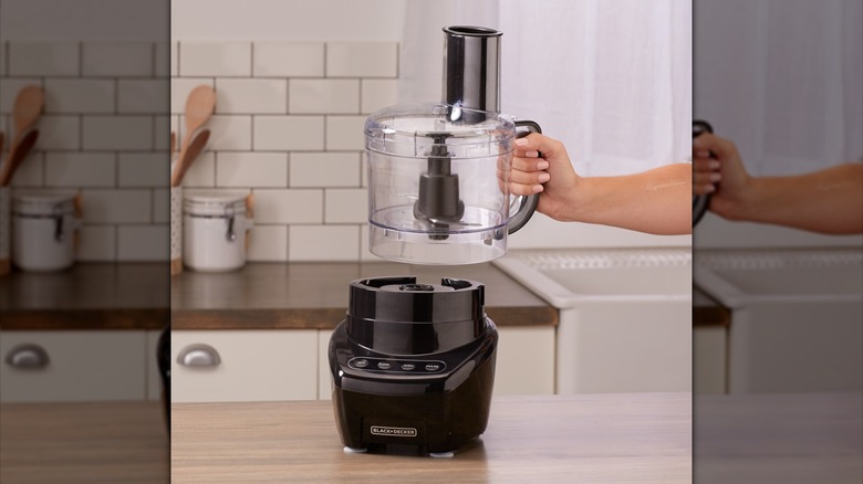 hand placing a Black + Decker food processor container on appliance base