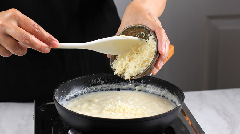 Hands pouring cheese into sauce