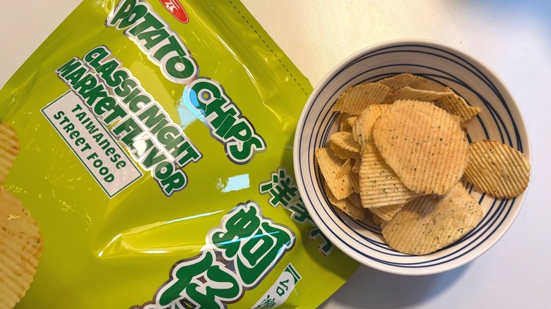 Bowl of potato chips next to green bag of Classic Night Market Flavor Potato Chips on white table