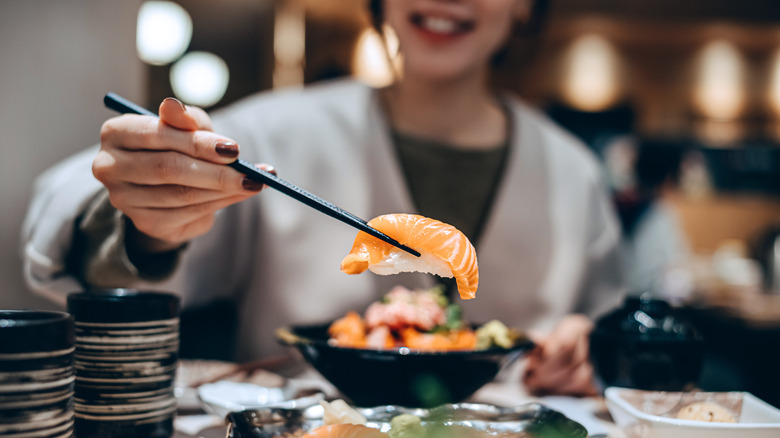 Smiling person picking up sushi with chopsticks