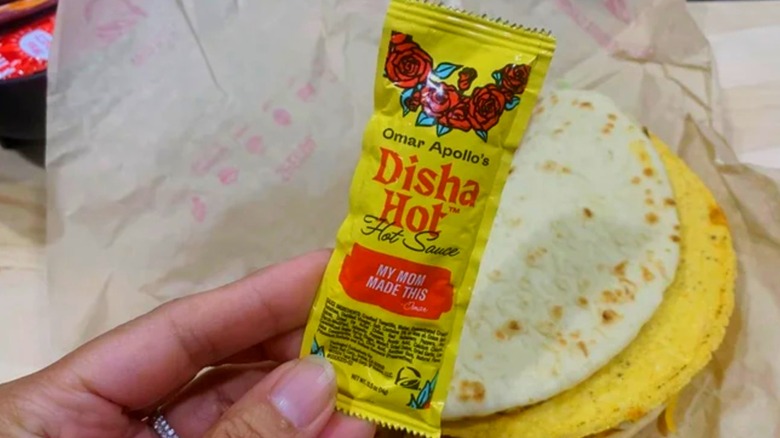 Woman's hand holding a Dish Hot Hot Sauce packet in front of a taco.