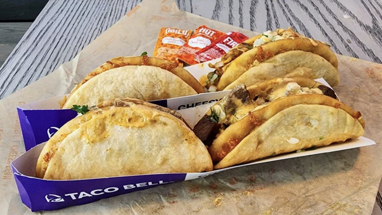 4 Taco Bell Cheesy Street Chalup in purple and white cartons on paper.