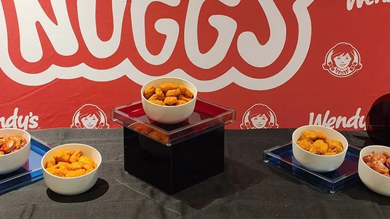 Wendy's saucy chicken nuggets in a white bowl on a glass case in front of Wendy's red and white backdrop.