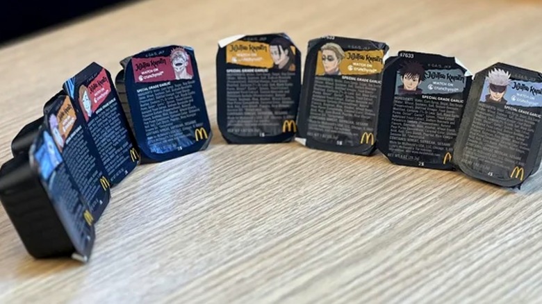 8 black packets of McDonald's Garlic Sauce with the faces of 8 Jujutsu Kaisen on them, one character face per packet.