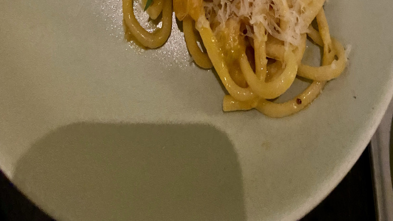 plate of bucatini pasta topped with a creamy sungold tomato sauce, freshly grated cheese, and garnished with small green and purple basil leaves