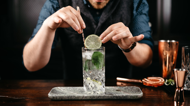 Bartender pouring and preparing gin and tonic with lime at bar counter. Details of mixology