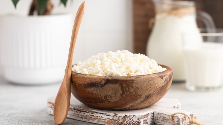 A wood bowl of cottage cheese with wood spoon on wood cutting board