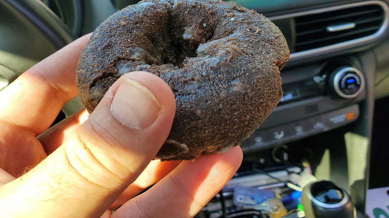 Person holding a chocolate cake donut in a car