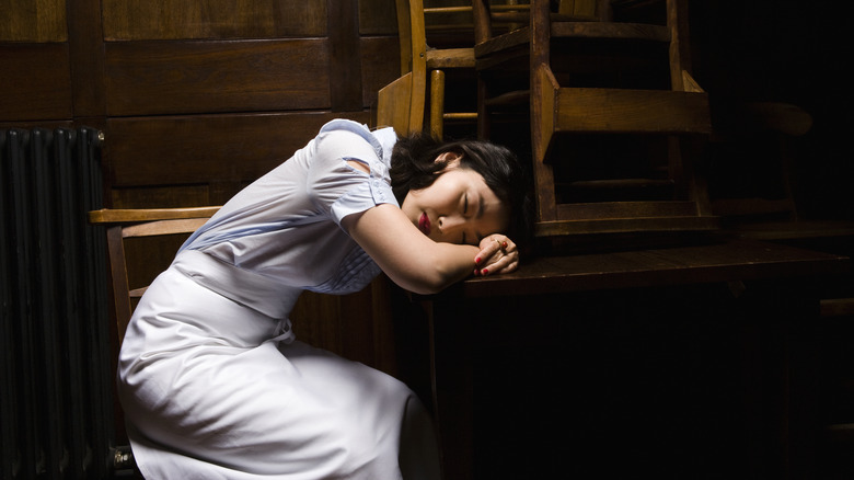 Restaurant server asleep in front of stacked chairs