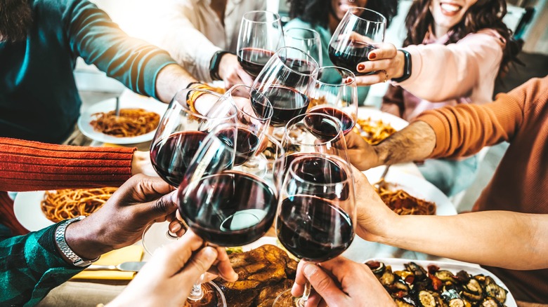 Group of patrons raising their red wine glasses for a toast