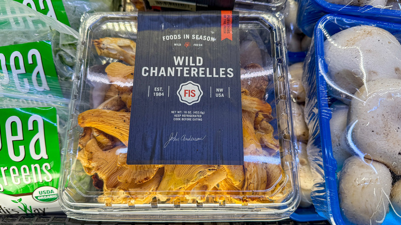 Plastic container of chanterelle mushrooms next to other mushrooms