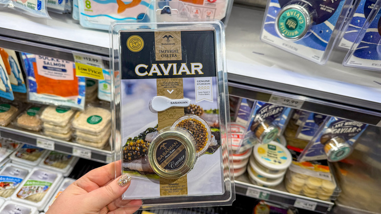 Hand holding package of caviar in front of grocery store shelves