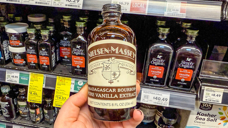 Hand holding jar of vanilla extract in front of vanilla extract bottles on grocery store shelf