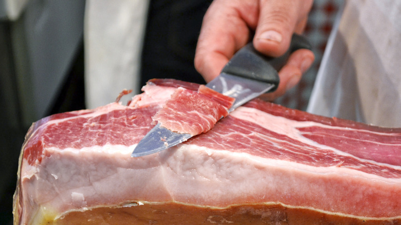 Knife cutting thin slice of Prosciutto di Parma