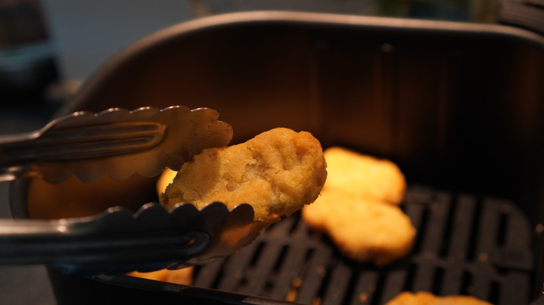 Tongs holding a chicken nugget in an air fryer