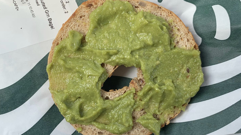 A Starbucks bagel half has avocado spread on top.