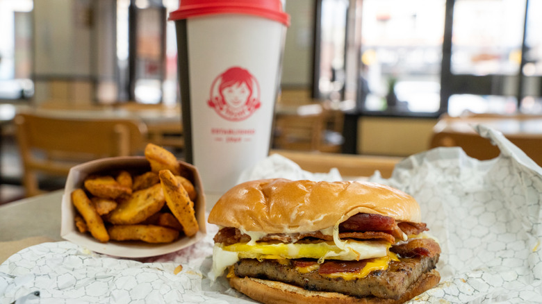 A Wendy's breakfast sandwich sits in front of a cup and a side of potatoes.