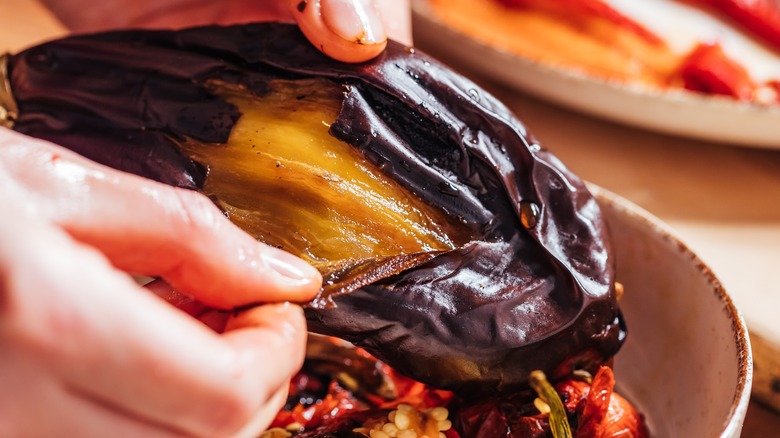 hand peeling a whole roasted eggplant