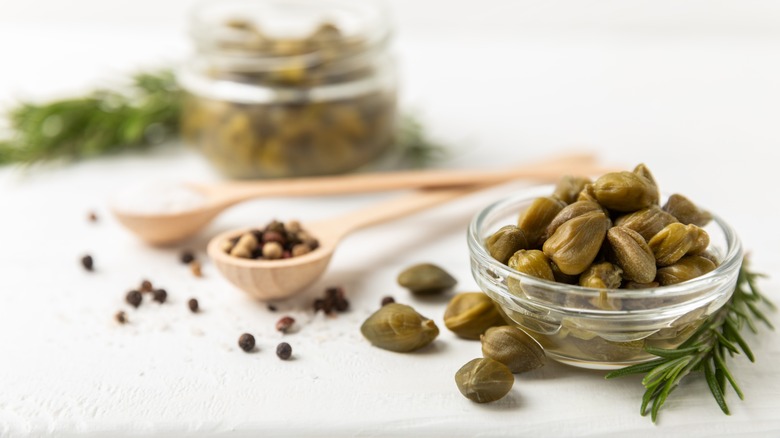 Capers in a glass bowl with rosemary and peppercorns