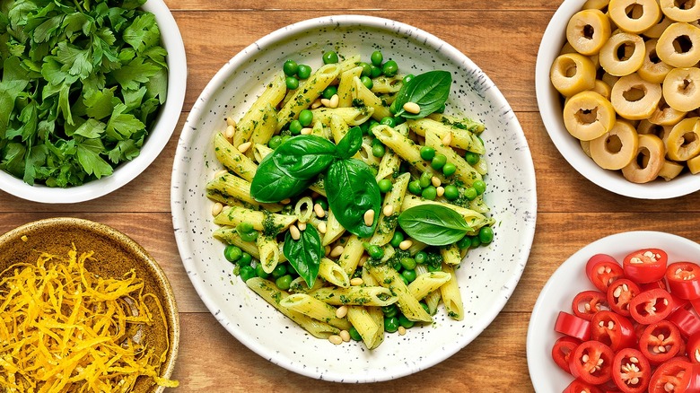 Pine, basil, and pea pasta surrounded by various pasta garnishes