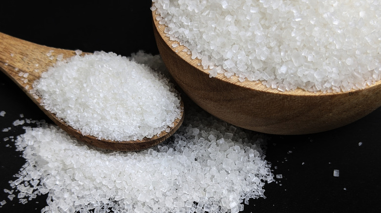 Granulated white sugar spilling out of a wooden bowl and spoon