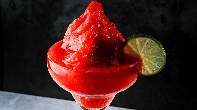 A close-up of a glass of a frozen strawberry daiquiri with a lime slice