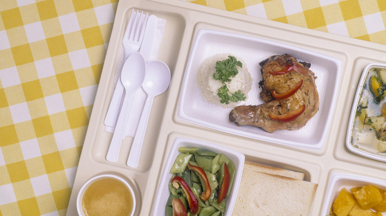 Cafeteria tray with meat, rice, and veg on yellow and white tablecloth