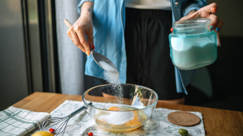 Person adding sugar to a bowl of eggs