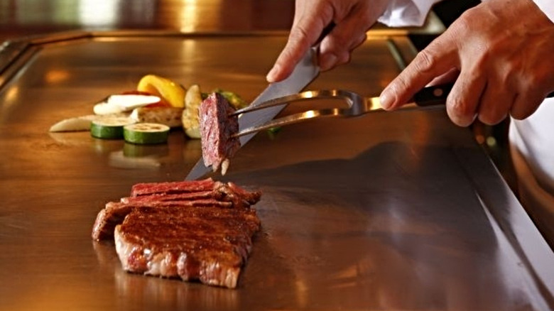 Chef slicing cooked meat at a hibachi station with veggies on the side