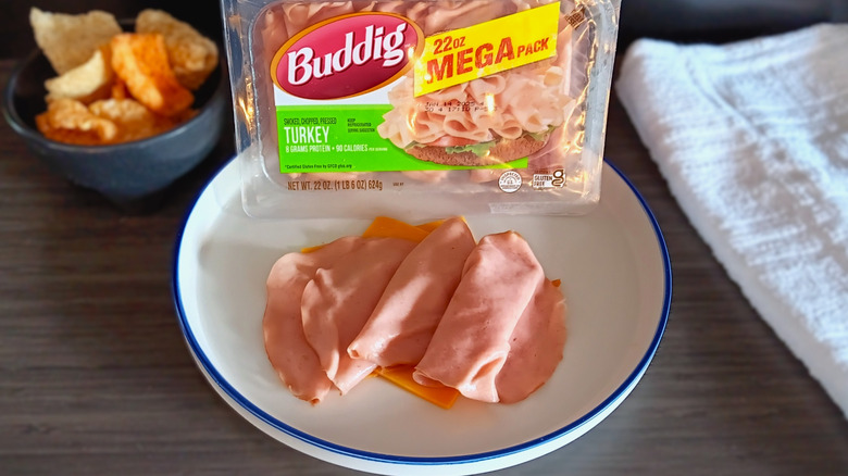 Buddig package of deli turkey with plate of turkey slices and pork rinds in background