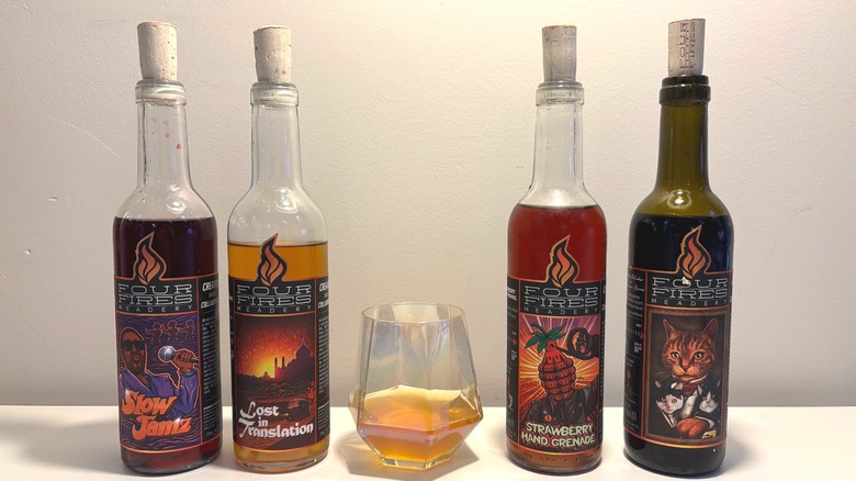 Four bottles and one glass of Four Fires mead on a white table