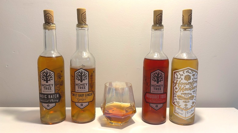 Four bottles and one glass of Honey Tree mead on a white table