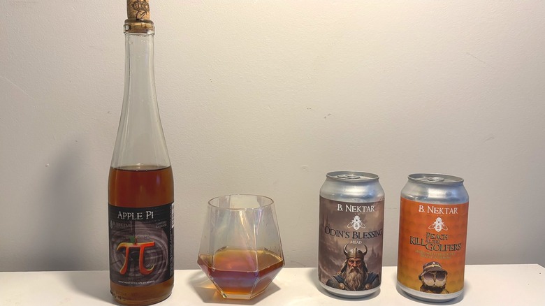 One bottle, two cans, and one glass of B. Nektar mead on a white background