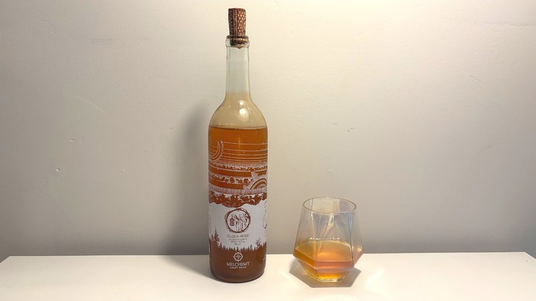 Bottle next to glass of Melchemy Craft Mead on a white table