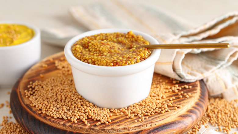 Grainy Dijon mustard in white bowl on a wooden trivet