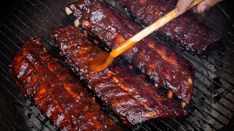 saucing ribs with barbecue sauce on the grill