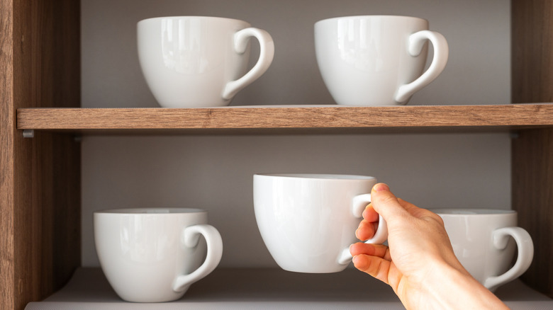 Hand placing white mug into shelf full of white mugs