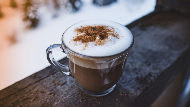 Cup of coffee sits on wooden railing against snowy backdrop