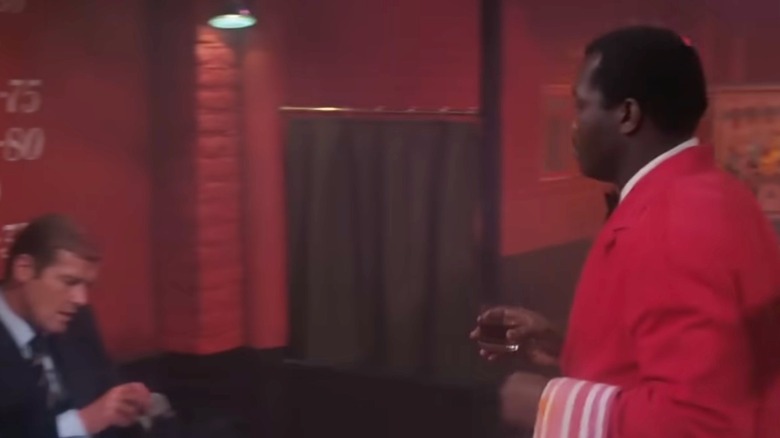 A waiter in a red jacket serving a glass of bourbon in Live and Let Die