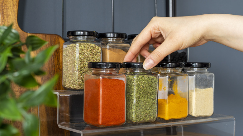 A hand selects a jar of herbs from a spice rack 