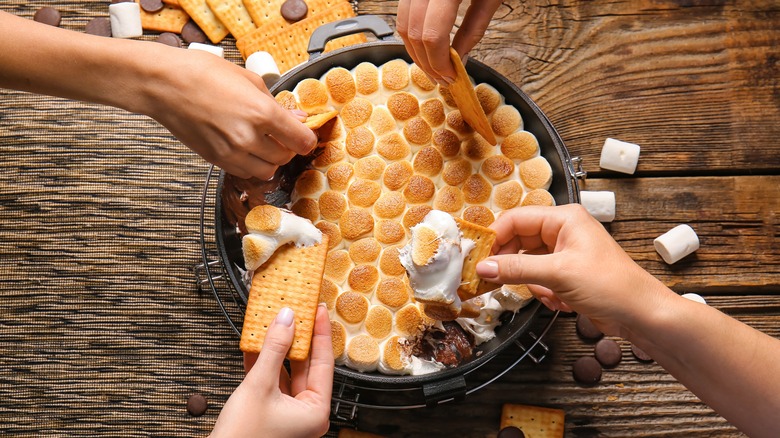 Hands dipping into s'mores skillet