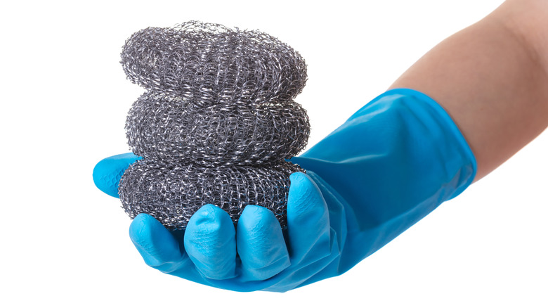 Gloved hand holding steel wool scrubbers