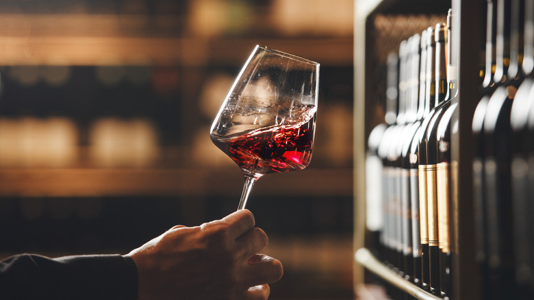 Hand holding wine close to shelf of wine bottles