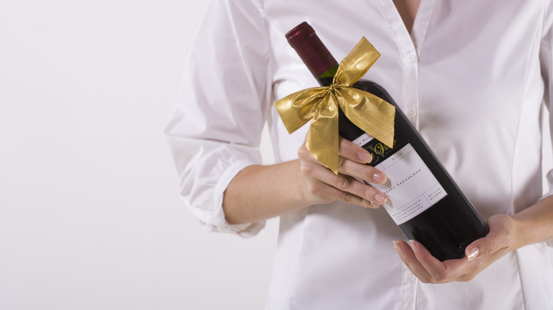 Faceless person holding wine bottle with gold bow on it