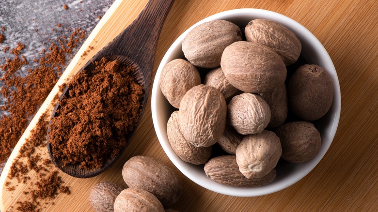 Nutmeg powder next to seeds in a bowl