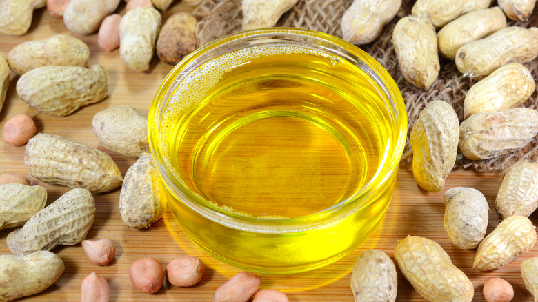 Peanut oil in a glass bowl with peanuts surrounding it