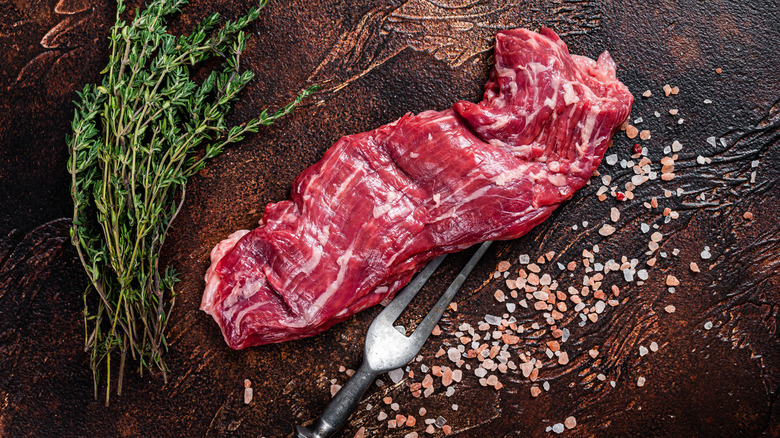 Raw skirt steak on cutting board with herbs and rock salt