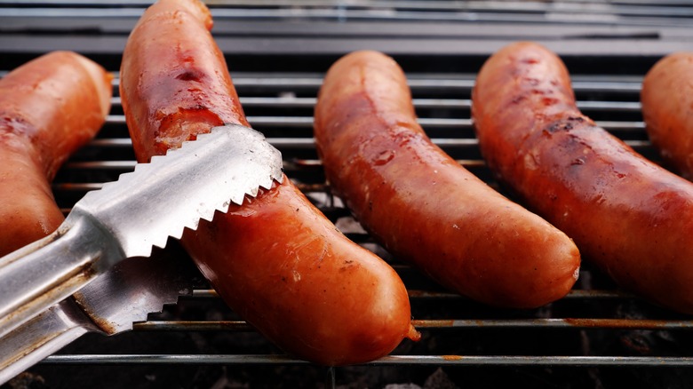 Person grilling sausages with tongs