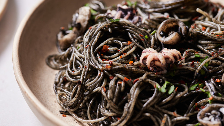 Bowl of cuttlefish ink pasta with red pepper flakes and squid